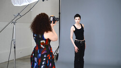 Photographer shooting a portrait of a woman in a studio with professional lighting setup.