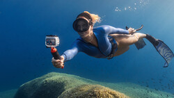 Snorkeler swimming horizontally above a large underwater boulder while holding an action camera.
