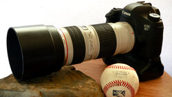 Canon EOS 6D DSLR camera with telephoto lens, baseball, and rock on wooden surface.