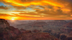 Grand Canyon landscape at sunset with golden light illuminating layered rock formations and deep shadows in the valleys.