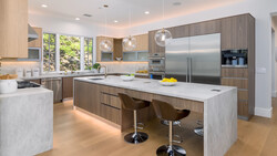 Modern kitchen with wood cabinetry, white quartz countertops, stainless steel appliances, and a large island with seating.