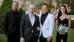 Four people in formal attire standing outdoors on a lawn with architectural backdrop.