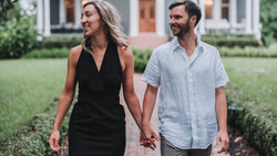 Couple walking hand-in-hand through a manicured garden in front of a residential home.
