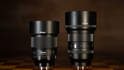 Two manual focus prime lenses side by side on a wooden surface against a brown background.