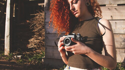 Woman with red curly hair holding vintage film camera outdoors.