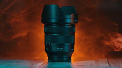 A dark telephoto zoom lens with a lens hood, photographed against a warm orange and cool teal background.