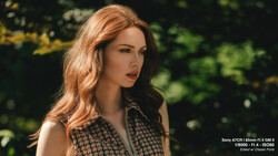 Woman with reddish-brown wavy hair looking to the side outdoors with blurred green foliage background.
