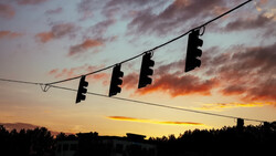 Multiple traffic lights silhouetted against a dramatic sunset sky with orange and golden clouds.