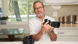 Photographer holding a camera with telephoto lens in a modern kitchen setting.
