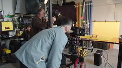 Filmmaker operating a cinema camera on a gimbal stabilizer in a studio with yellow backdrop and lighting equipment.