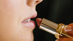 Close-up of lips with gold-toned lipstick applicator positioned near mouth.