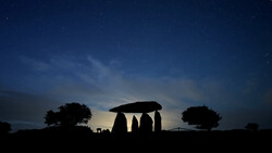 Silhouette of ancient stone monument against twilight sky with stars and surrounding trees.