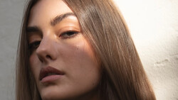 Woman with long brown hair gazing downward in soft, directional lighting.