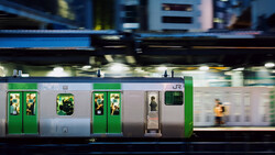 Motion-blurred train with green and silver livery moving through an urban station at dusk.