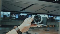 Person holding a vintage rangefinder camera with leather strap in an indoor terminal or station setting.