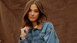 Woman wearing a denim shirt with corduroy collar against a brown fabric backdrop.