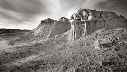 Dramatic rock formations and eroded cliffs in an arid landscape under stormy skies.