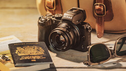 Nikon camera with lens surrounded by travel accessories including passport, sunglasses, and leather bag.