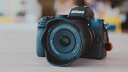 Nikon mirrorless camera with blue body and standard zoom lens on neutral surface.