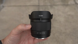 Hand holding a Viltrox AF 15/1.7 E lens with hood attached against a concrete background.