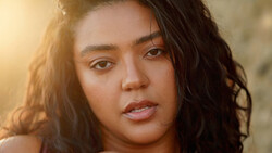 Portrait of a woman with long dark wavy hair, looking directly at camera with warm golden hour lighting.