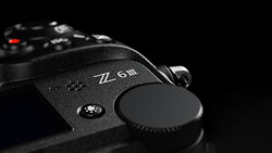 Close-up of a mirrorless camera body showing control dial and lens cap against black background.