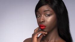 Woman with long black hair and red lipstick gazing downward against neutral background.
