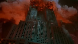 Art Deco skyscraper engulfed in flames and orange smoke against a dark sky.