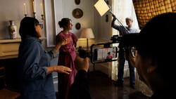 Behind-the-scenes film production in an elegant interior with crew operating camera and lighting equipment.