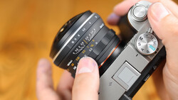 Hands holding a vintage rangefinder camera with an interchangeable lens mounted on top.