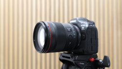 Canon DSLR camera mounted on tripod with telephoto lens against corrugated metal backdrop.