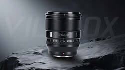 Black camera lens with manual focus ring and depth-of-field scale mounted on rocky surface.
