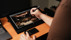 Digital artist using stylus on tablet displaying warm-toned landscape image with golden lighting.