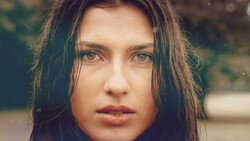 Woman with long dark hair looking directly at camera with neutral expression.