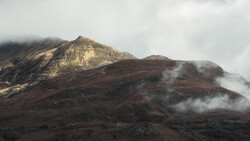 Volcanic mountain with golden-lit peak and dark slopes partially shrouded in white steam and clouds.