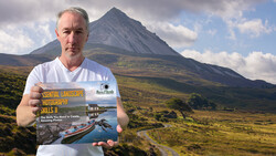 Photographer holding a landscape photography instructional book with a dramatic conical mountain and moorland in the background.