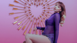 Woman in purple outfit posing against pink background with gold arrow wall decoration.