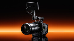 Professional cinema camera rig with prime lens, external monitor, and microphone mounted on top against warm orange gradient backdrop.