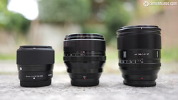Three black camera lenses arranged in size progression on concrete surface outdoors.
