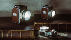 Three vintage film cameras with illuminated lenses arranged on antique leather-bound books against a textured wall.