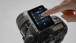 Hand touching smartphone screen displaying camera exposure settings mounted on DSLR camera body.
