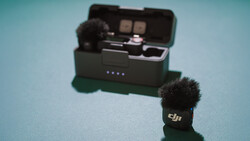 DJI wireless microphone with windscreen next to its charging case on a blue background.