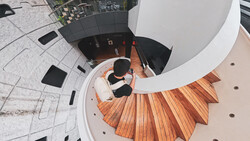 Overhead view of a curved staircase with wooden treads descending into a dark interior space.