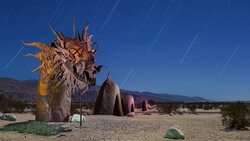 Large wooden dragon sculpture with elaborate carved details stands in a desert landscape under a starry night sky.