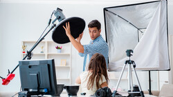 Two people adjusting a large softbox light modifier in a home photography studio setup.