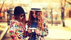 Two women wearing colorful floral blazers and sunglasses standing outdoors in a park.