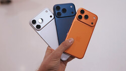 Three smartphone cases in white, dark blue, and orange held in a hand, displaying triple-lens camera modules.