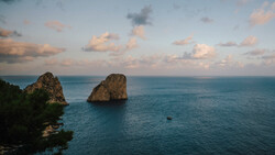 Two tall rock formations rise from turquoise water at sunset, with a small boat visible in the distance.
