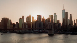 Manhattan skyline at golden hour with waterfront and bridge in foreground.