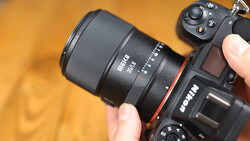 Prime lens mounted on mirrorless camera body held in hands against warm yellow background.